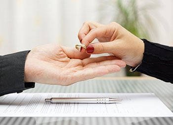 Image representing hands exchanging ring over contracts and marriage agreement- Aminu Law Firm, PLLC