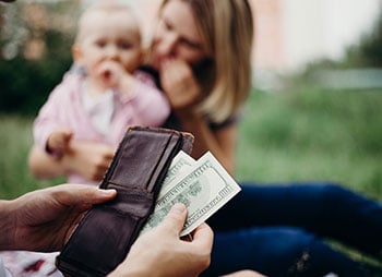 A woman holds a baby and a wallet, reflecting unemployment and child support - Aminu Law Firm, PLLC